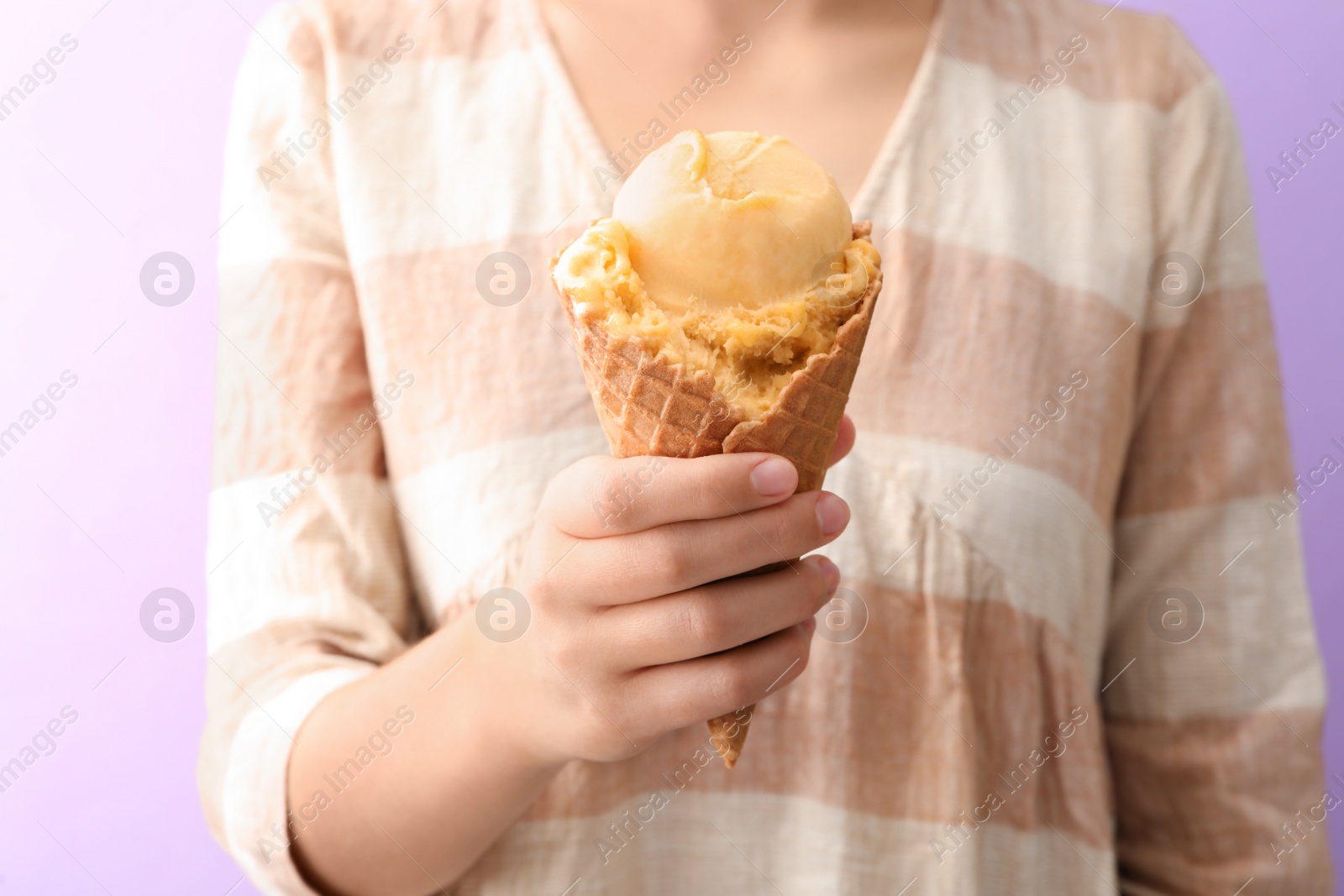 Photo of Woman holding yellow ice cream in wafer cone on violet background, closeup