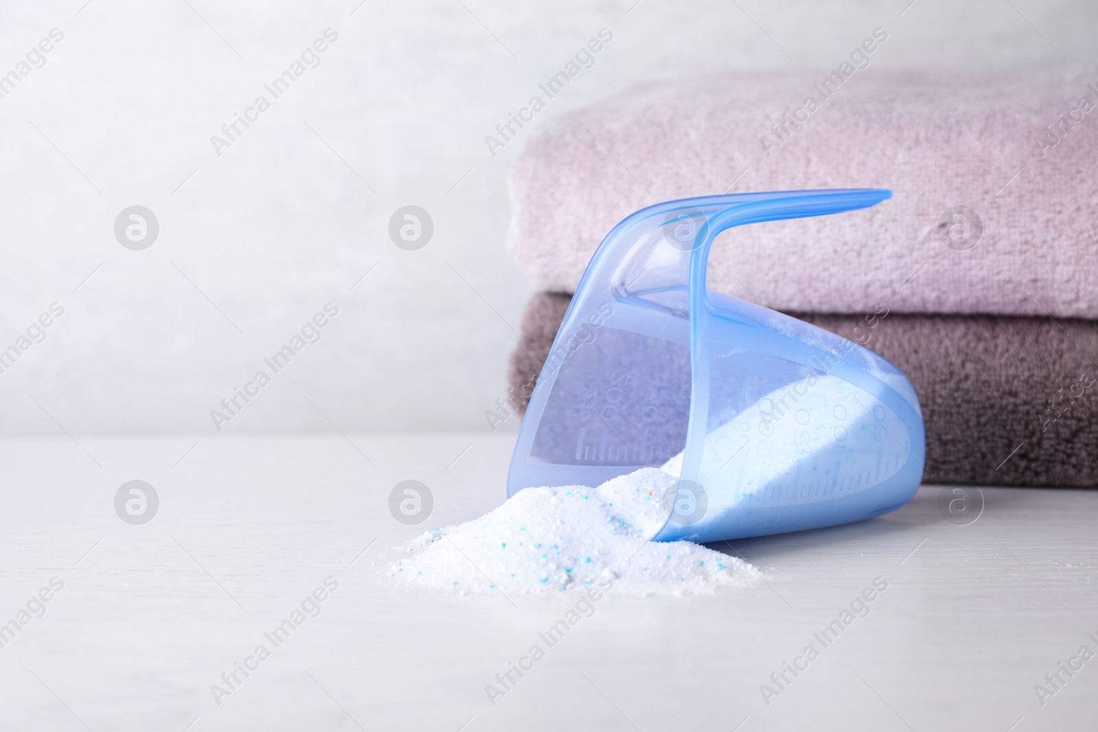 Photo of Measuring cup and scattered laundry powder near towels on table, space for text