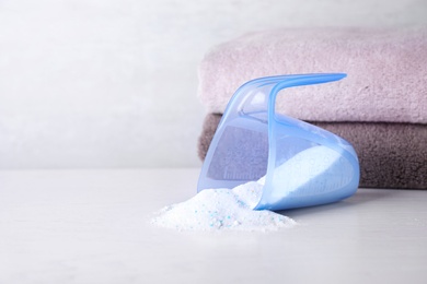 Photo of Measuring cup and scattered laundry powder near towels on table, space for text