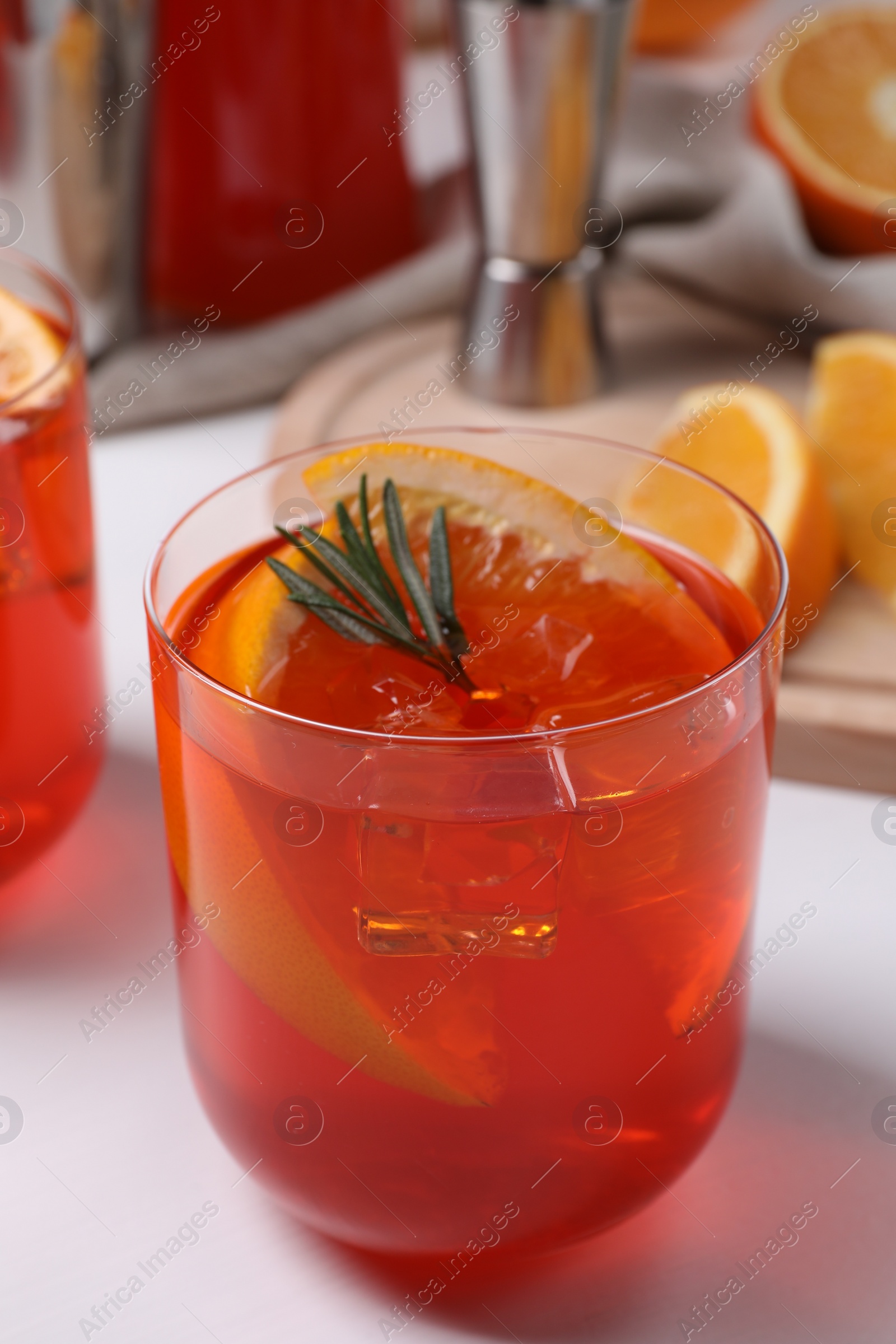 Photo of Aperol spritz cocktail, ice cubes, rosemary and orange slices in glass on white wooden table, closeup