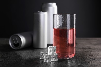 Energy drink in glass, aluminium cans and ice cubes on grey table. Space for text