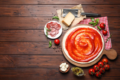 Photo of Flat lay composition with base and ingredients on wooden table, space for text. Pepperoni pizza recipe