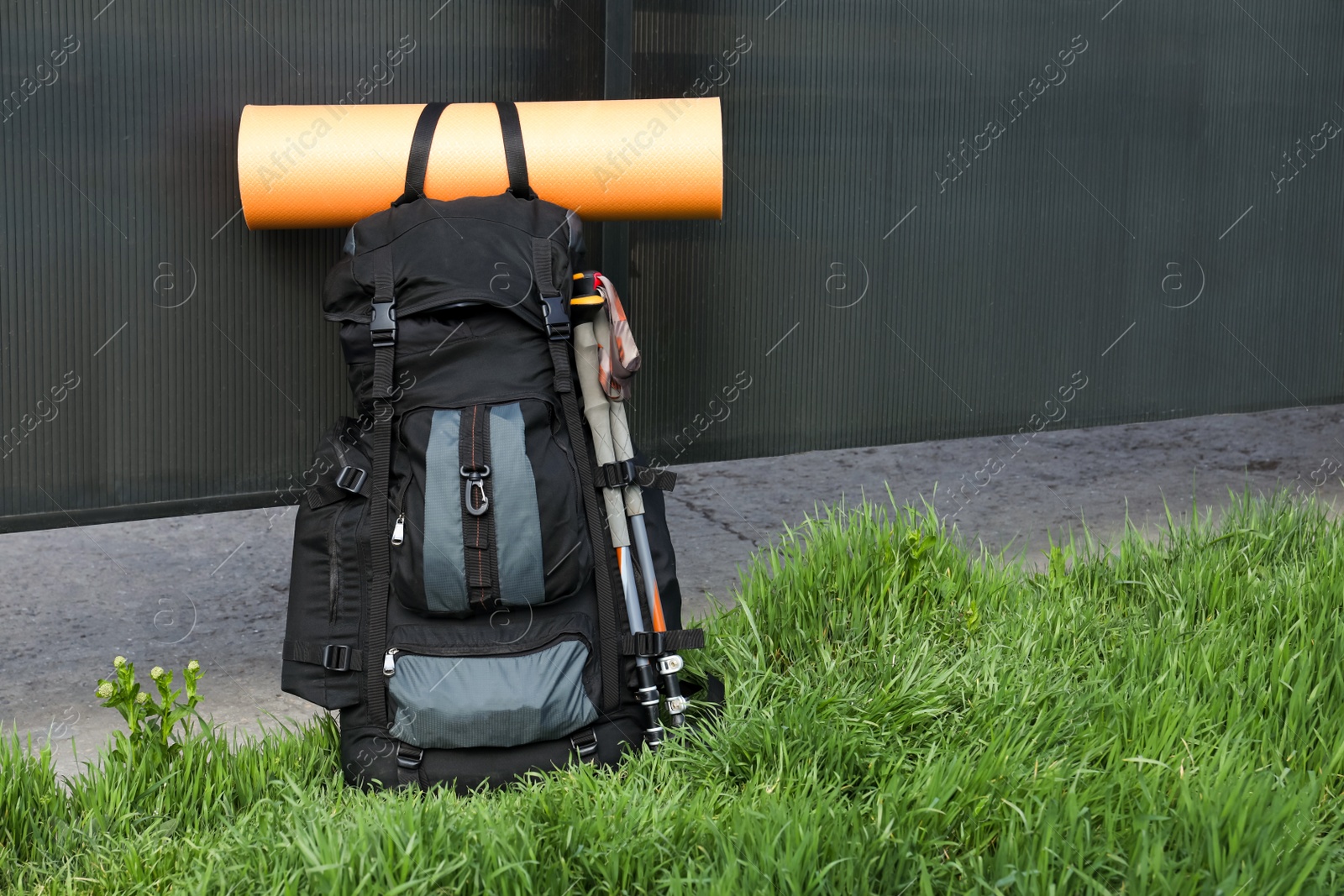 Photo of Backpack with trekking poles and camping mat on green grass. Space for text