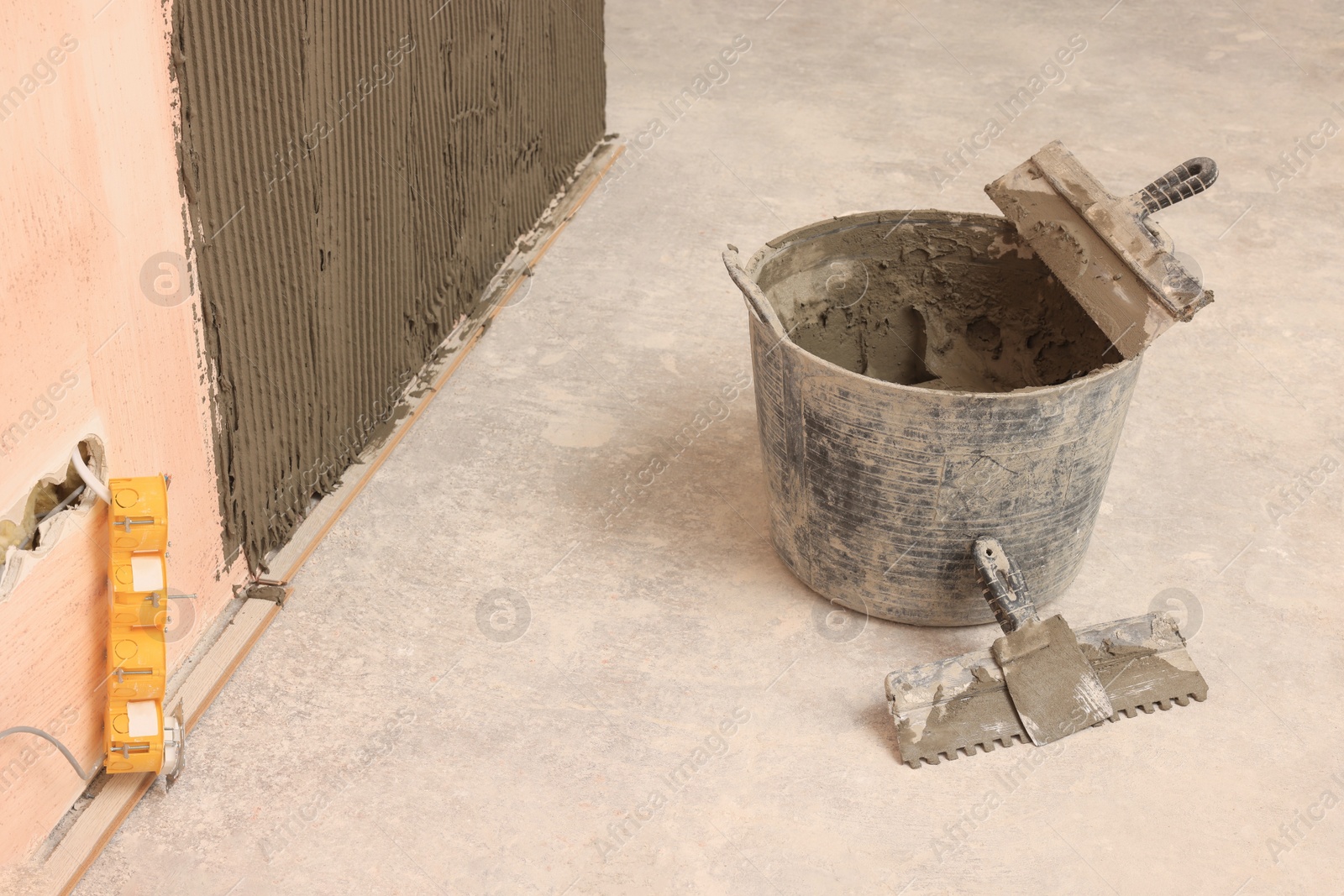 Photo of Bucket near white wall with adhesive mix for tile installation indoors