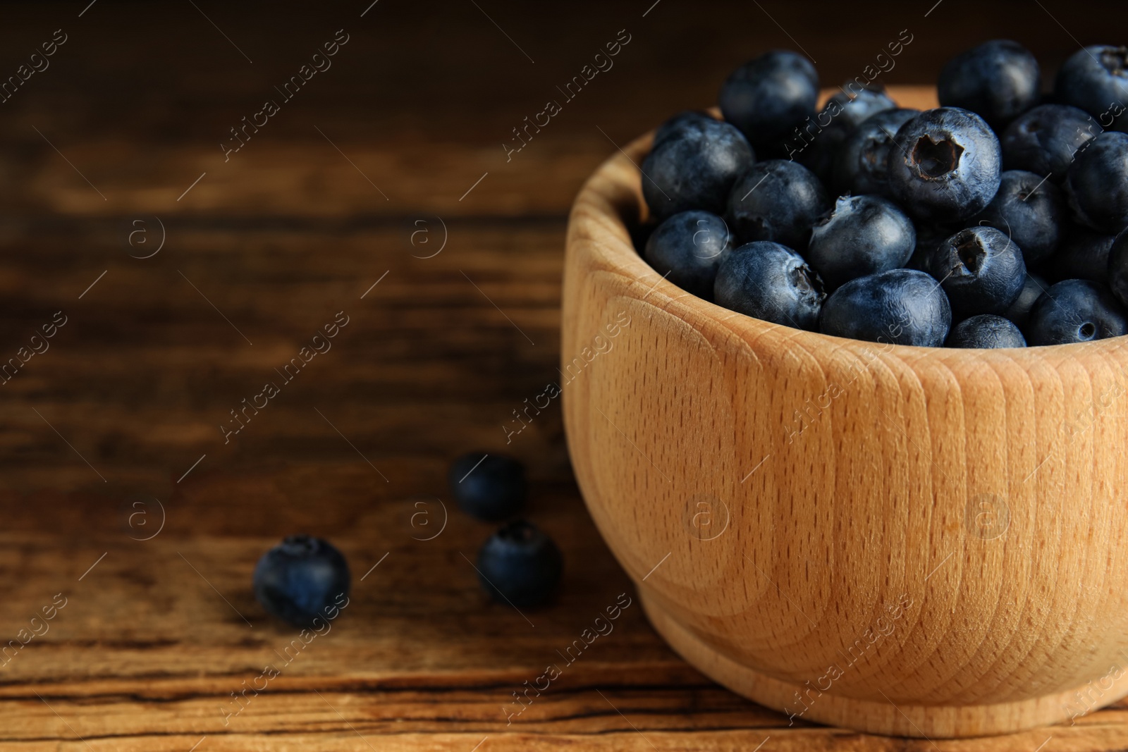 Photo of Fresh ripe blueberries in bowl on wooden table, closeup. Space for text