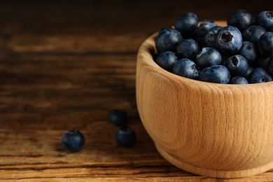 Photo of Fresh ripe blueberries in bowl on wooden table, closeup. Space for text