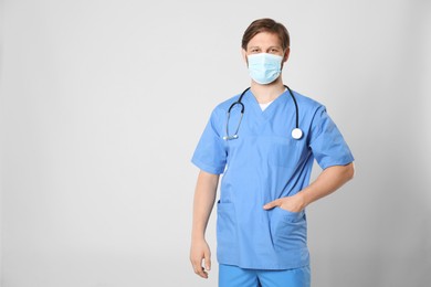 Doctor or medical assistant (male nurse) with protective mask and stethoscope on light grey background. Space for text