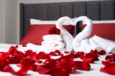 Photo of Honeymoon. Swans made with towels and beautiful rose petals on bed in room