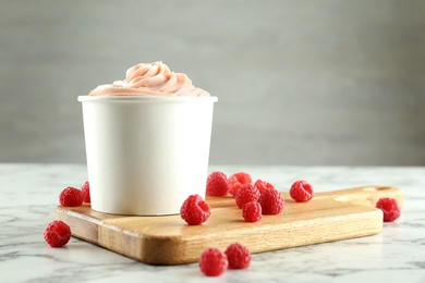 Cup with tasty frozen yogurt and raspberries on marble table. Space for text