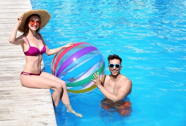 Happy young couple with inflatable ball at swimming pool