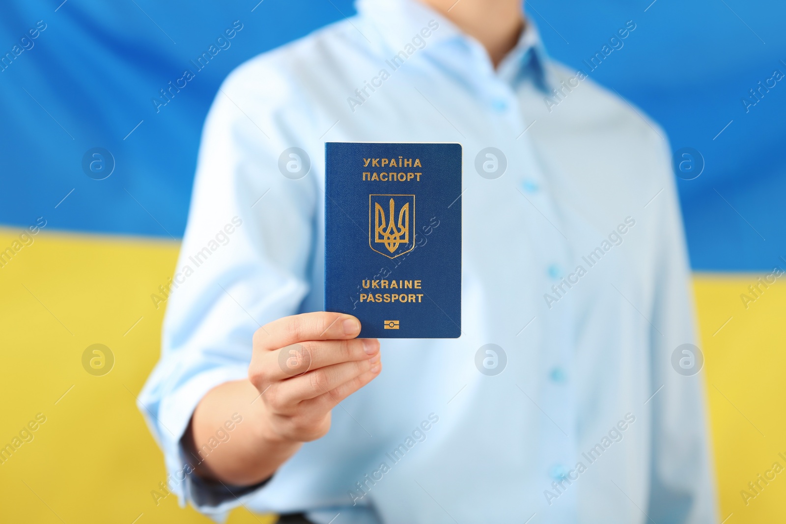 Photo of Woman holding Ukrainian travel passport against national flag, closeup. International relationships