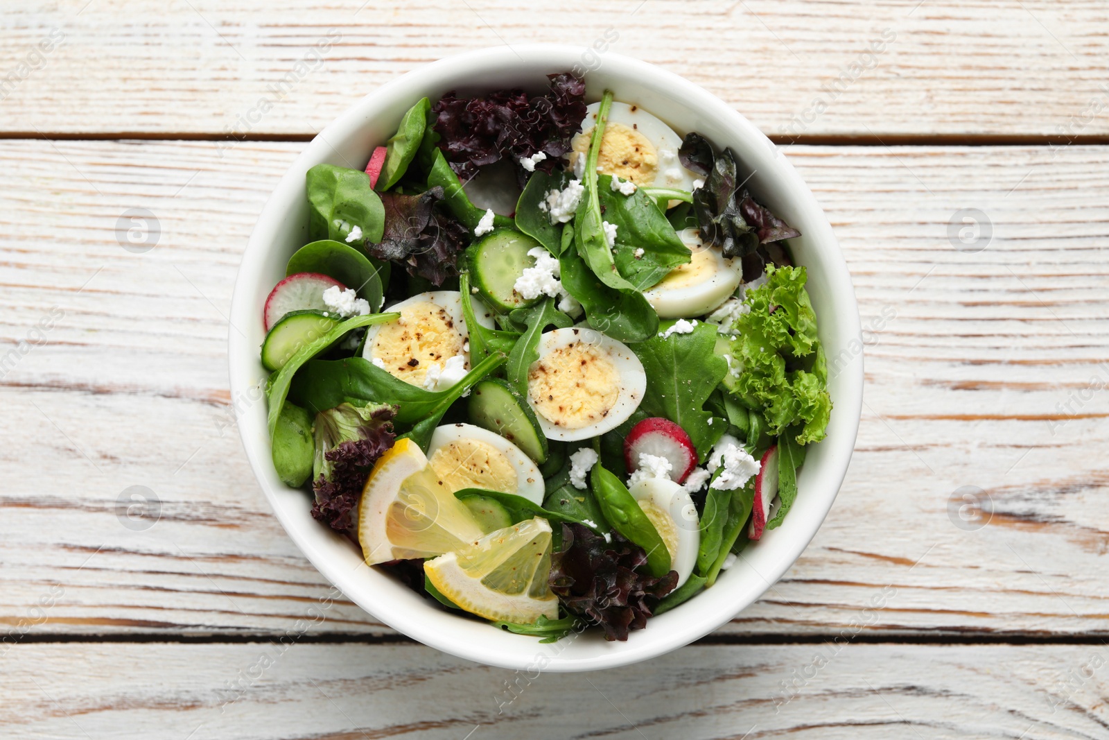 Photo of Delicious salad with boiled eggs, vegetables and lemon in bowl on white wooden table, top view