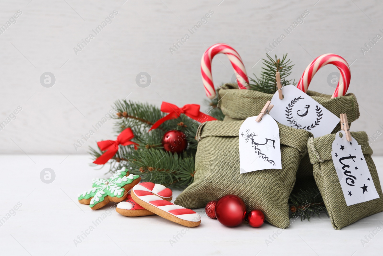 Photo of Bags with gifts, cookies and festive decor on white table, space for text. Christmas advent calendar