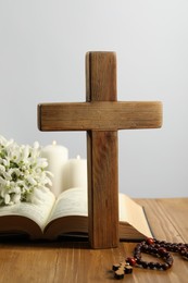 Photo of Cross, Bible, rosary beads, flowers and church candles on wooden table against light background