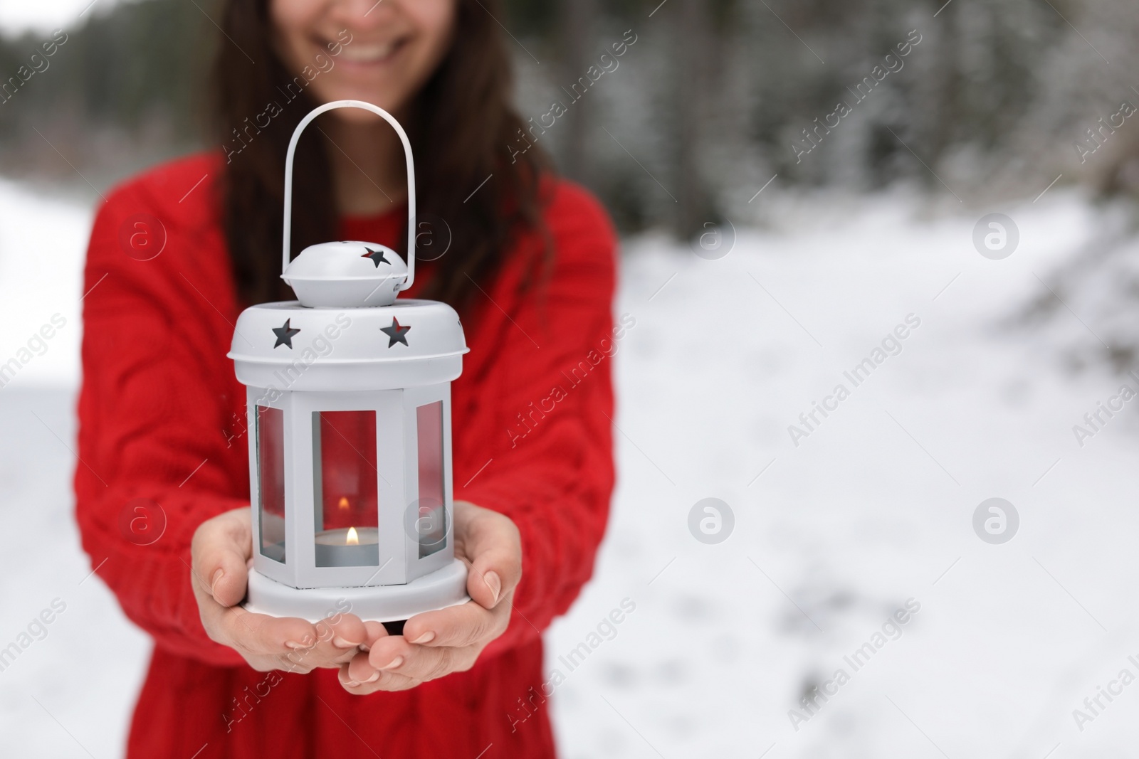 Photo of Woman holding lantern with burning candle near snowy forest. Space for text