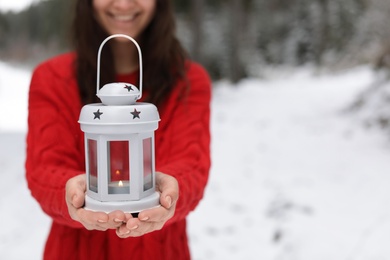 Woman holding lantern with burning candle near snowy forest. Space for text