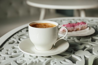 Photo of Cup of delicious aromatic coffee and eclair on table indoors