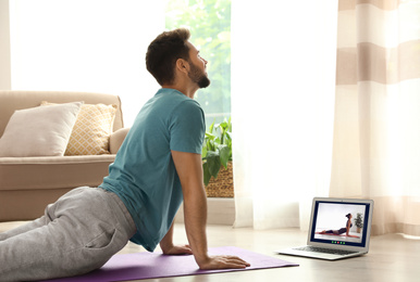 Image of Distance yoga course during coronavirus pandemic. Man having online practice with instructor via laptop at home