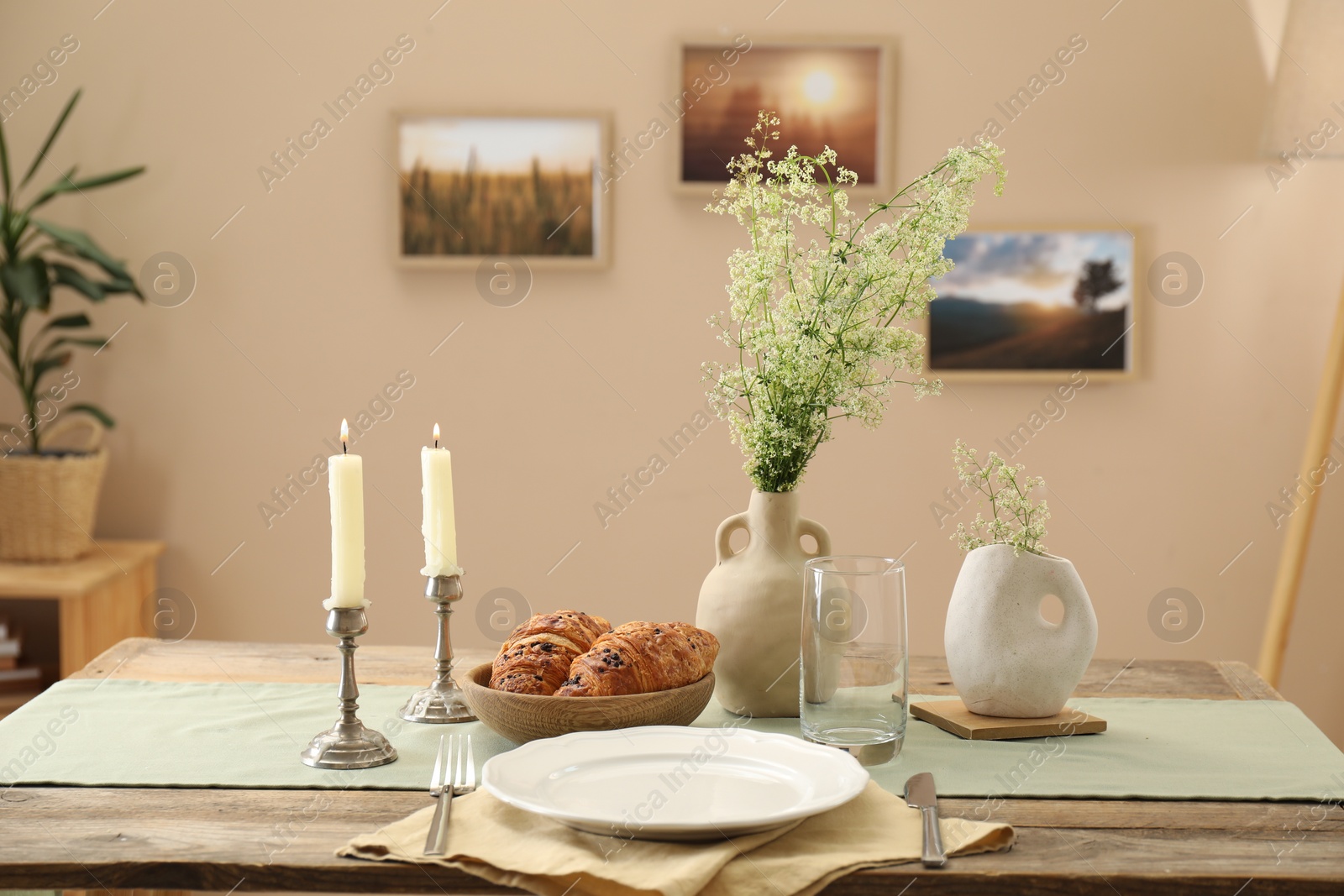 Photo of Clean tableware, candlesticks, flowers and fresh pastries on table in stylish dining room