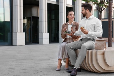 Photo of Happy colleagues having business lunch together on bench outdoors