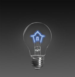 Image of Light bulb with tungsten filament in shape on house on dark background. Energy efficiency, loan, property or business idea concepts