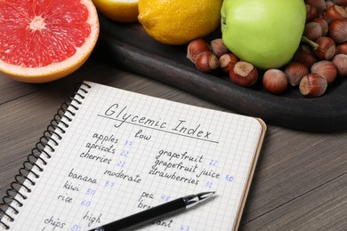 Notebook with products of low, moderate and high glycemic index, pen and food on wooden table, closeup