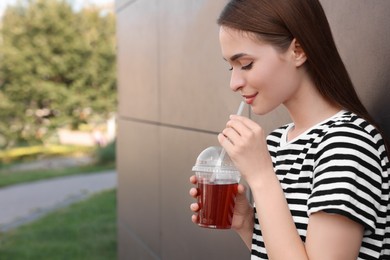 Photo of Young woman with plastic cup of fresh juice outdoors, space for text