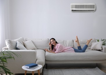 Image of Young woman resting under air conditioner on white wall at home