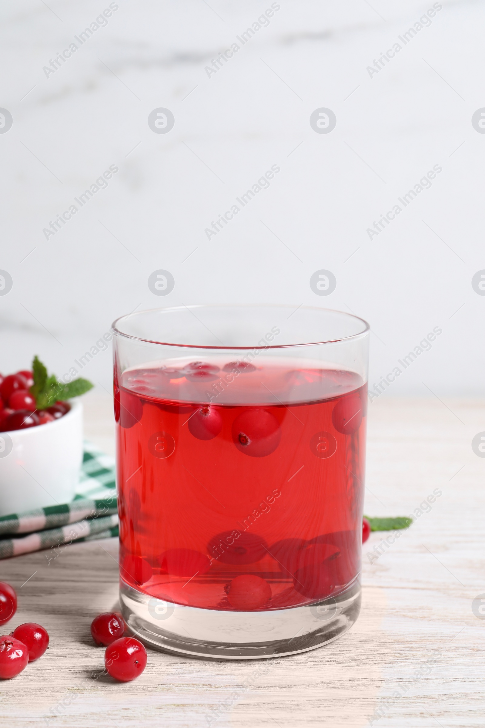 Photo of Tasty cranberry juice in glass and fresh berries on white wooden table
