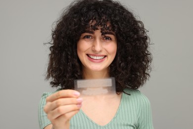 Photo of Young woman holding teeth whitening strips on grey background