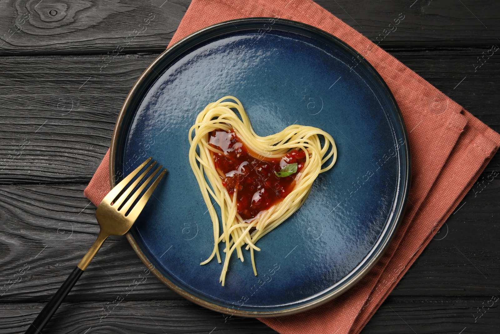 Photo of Heart made with spaghetti and sauce on black wooden table, top view