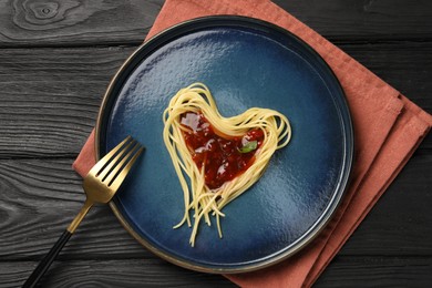 Heart made with spaghetti and sauce on black wooden table, top view