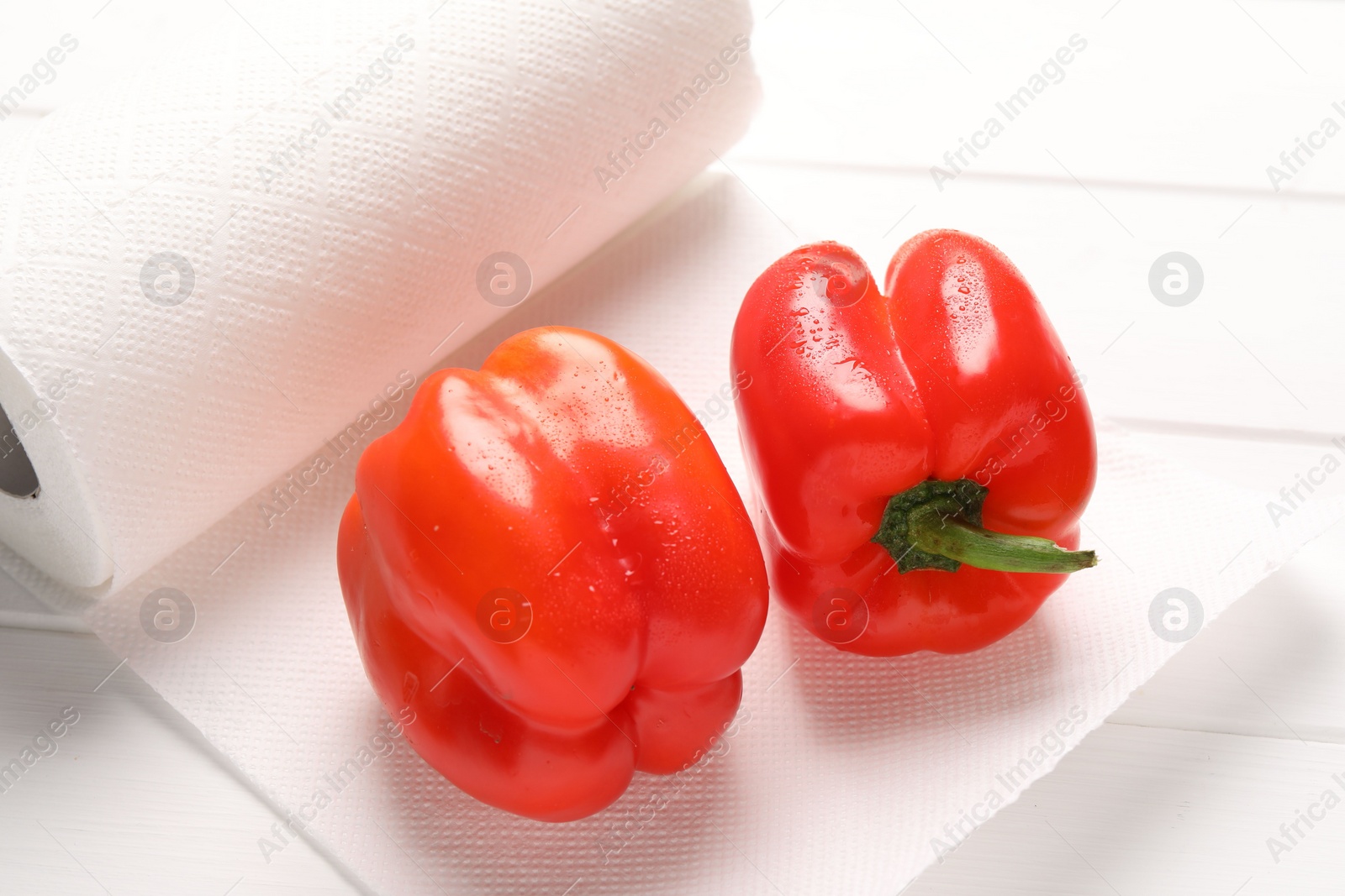 Photo of Roll of paper towels with wet bell peppers on white wooden table, closeup