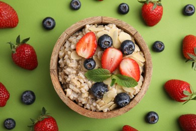 Photo of Tasty oatmeal with strawberries, blueberries and almond petals in bowl surrounded by fresh berries on green background, flat lay