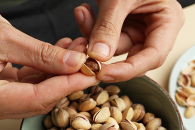 Photo of Woman opening tasty roasted pistachio nut at table, closeup