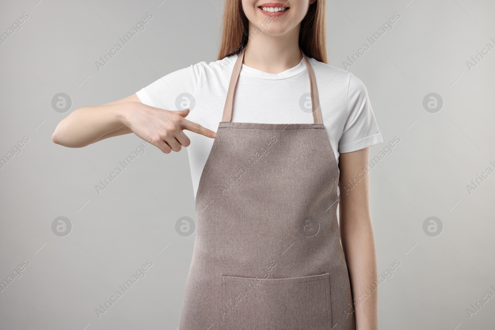 Photo of Woman pointing at kitchen apron on grey background, closeup. Mockup for design