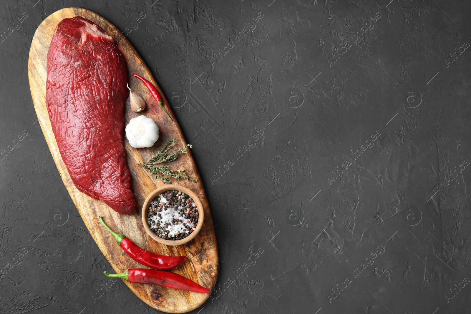 Photo of Piece of raw beef meat, products and spices on dark textured table, top view. Space for text