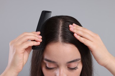 Woman with comb examining her hair and scalp on grey background, closeup