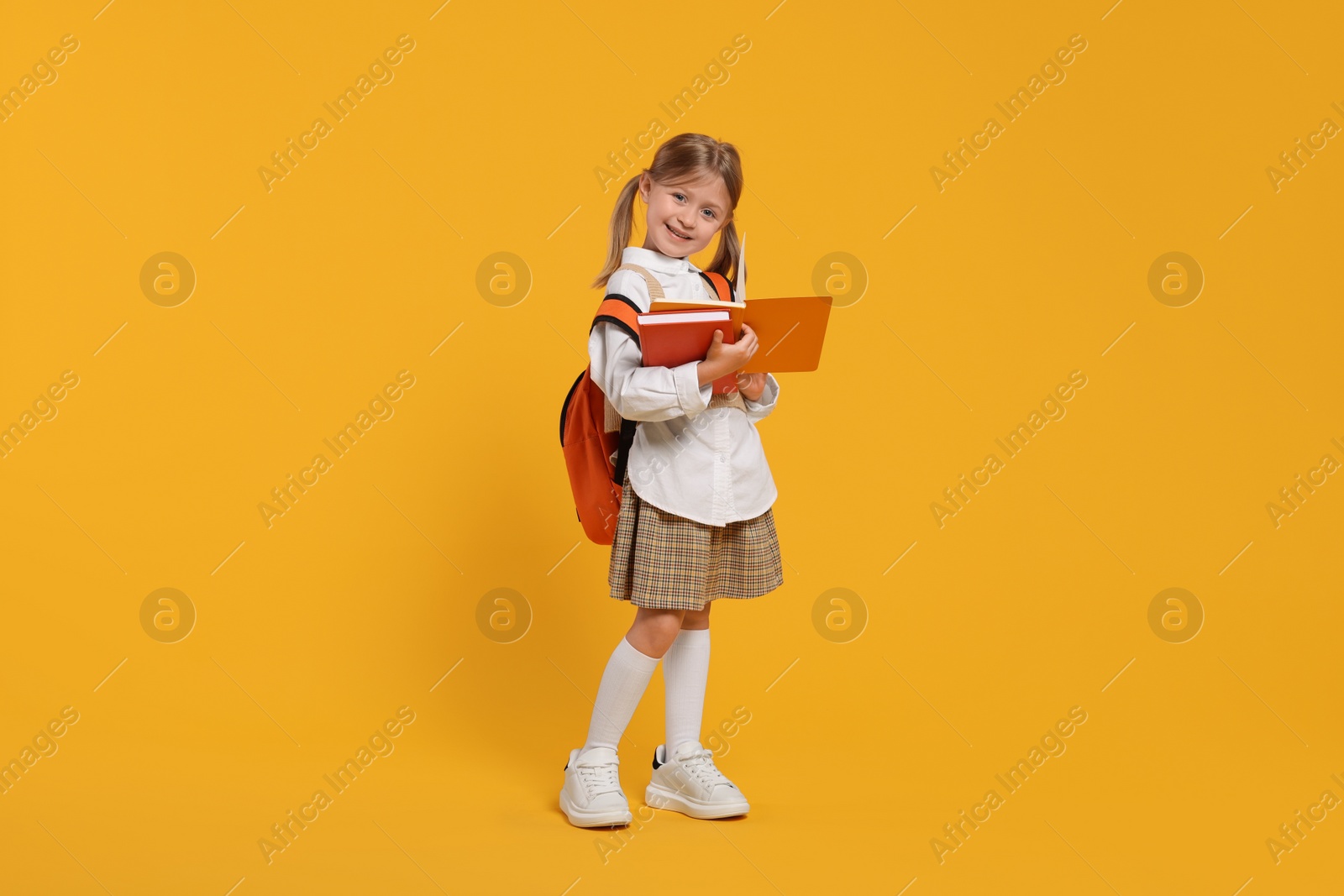 Photo of Happy schoolgirl with backpack and books on orange background