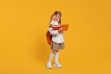 Happy schoolgirl with backpack and books on orange background