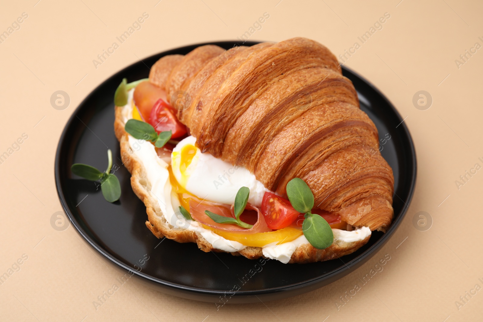 Photo of Tasty croissant with fried egg, tomato and microgreens on beige background, closeup