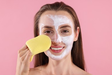 Happy young woman washing off face mask with sponge on pink background