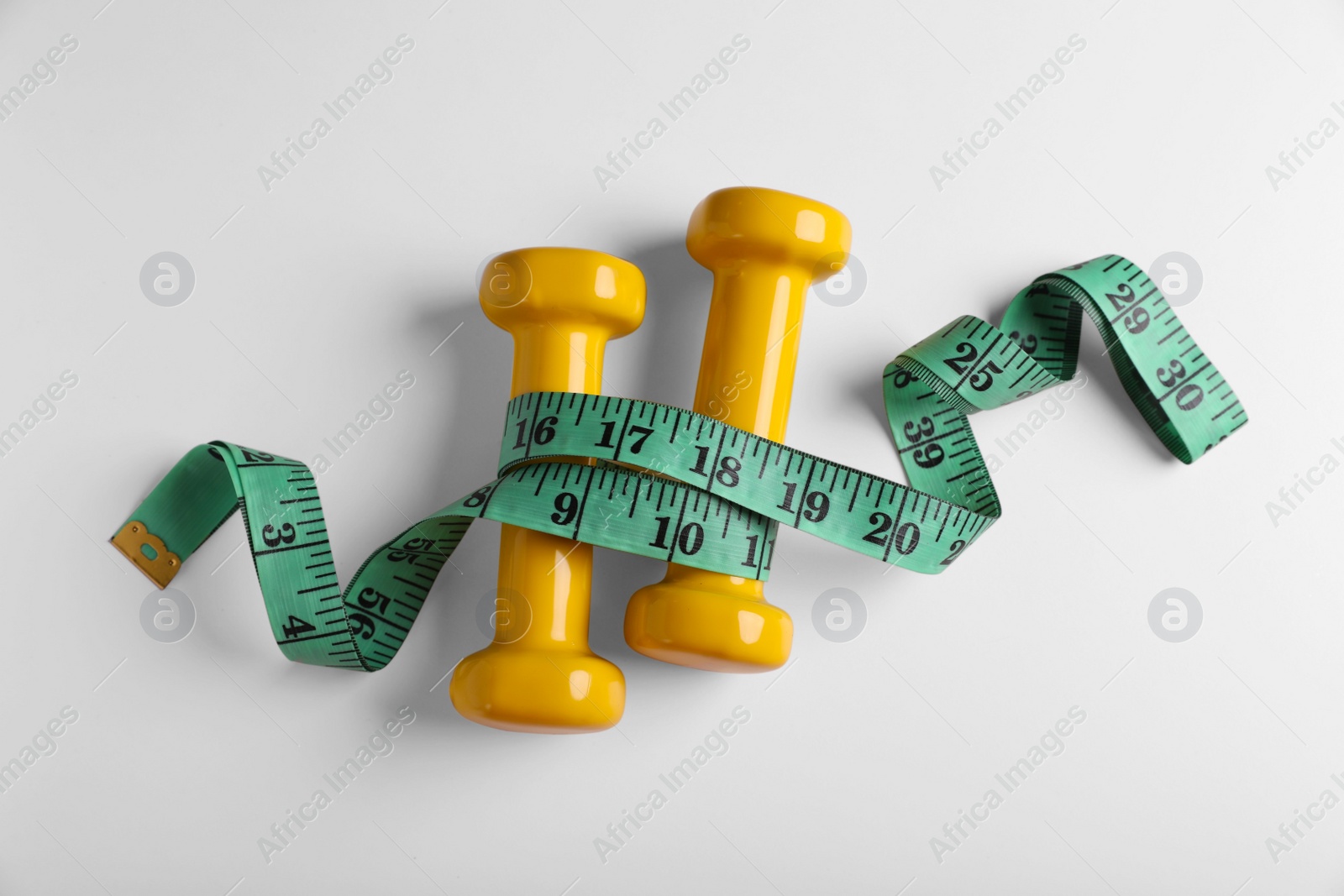 Photo of Measuring tape and dumbbells on white background, flat lay. Weight control concept