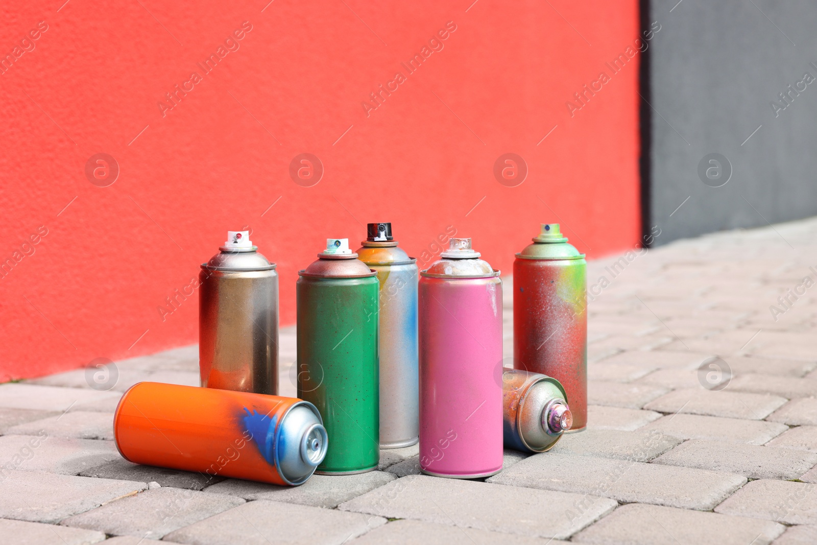 Photo of Cans of different spray paints on pavement near wall