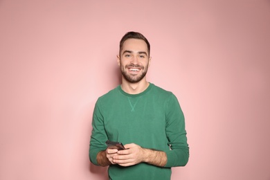 Handsome young man with mobile phone on color background