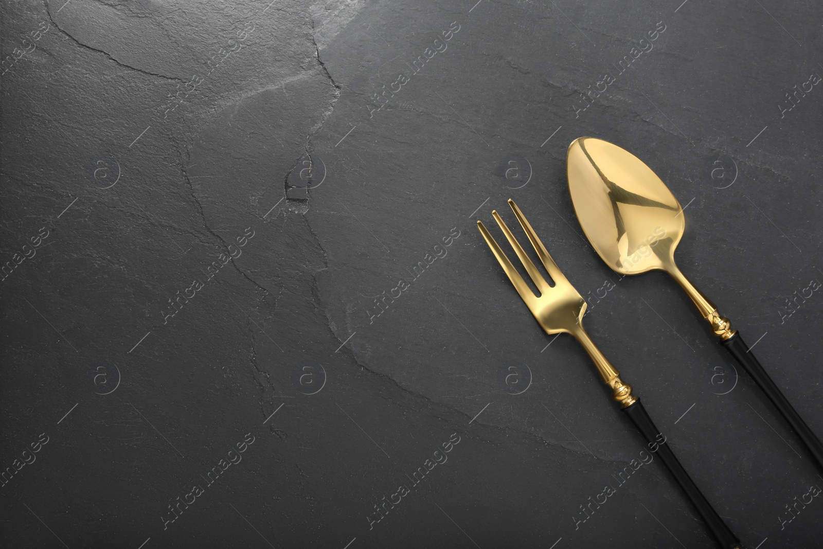 Photo of Shiny fork and spoon on black table, flat lay. Space for text