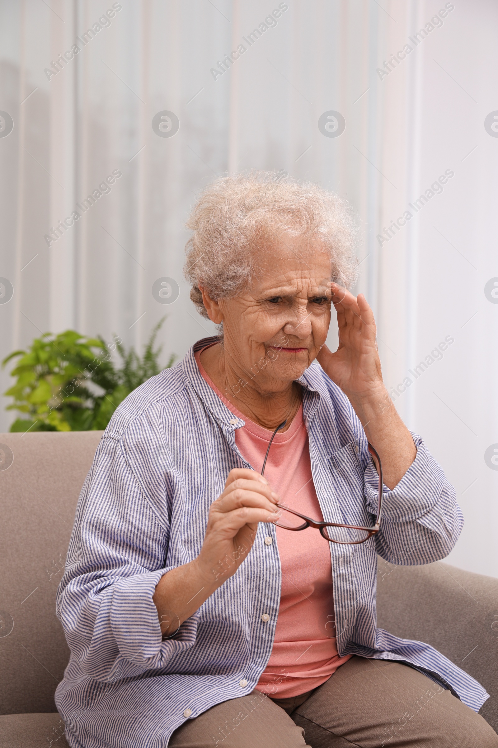 Photo of Senior woman with headache sitting on sofa at home