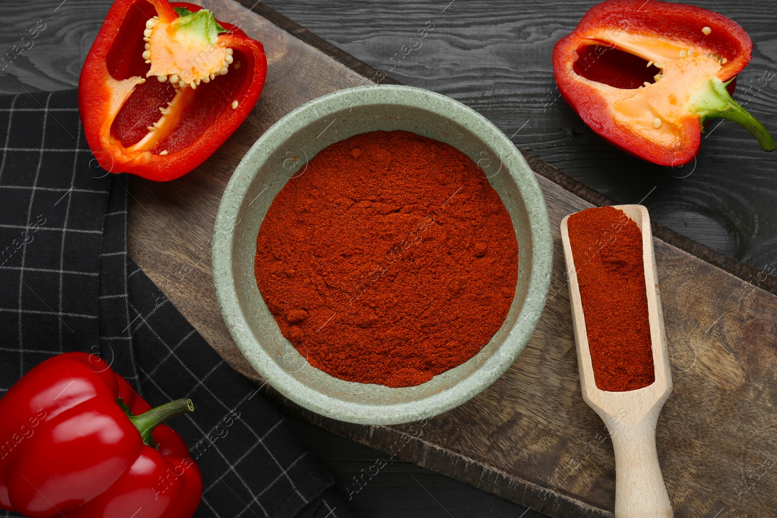 Photo of Bowl of aromatic paprika and fresh peppers on black wooden table, flat lay