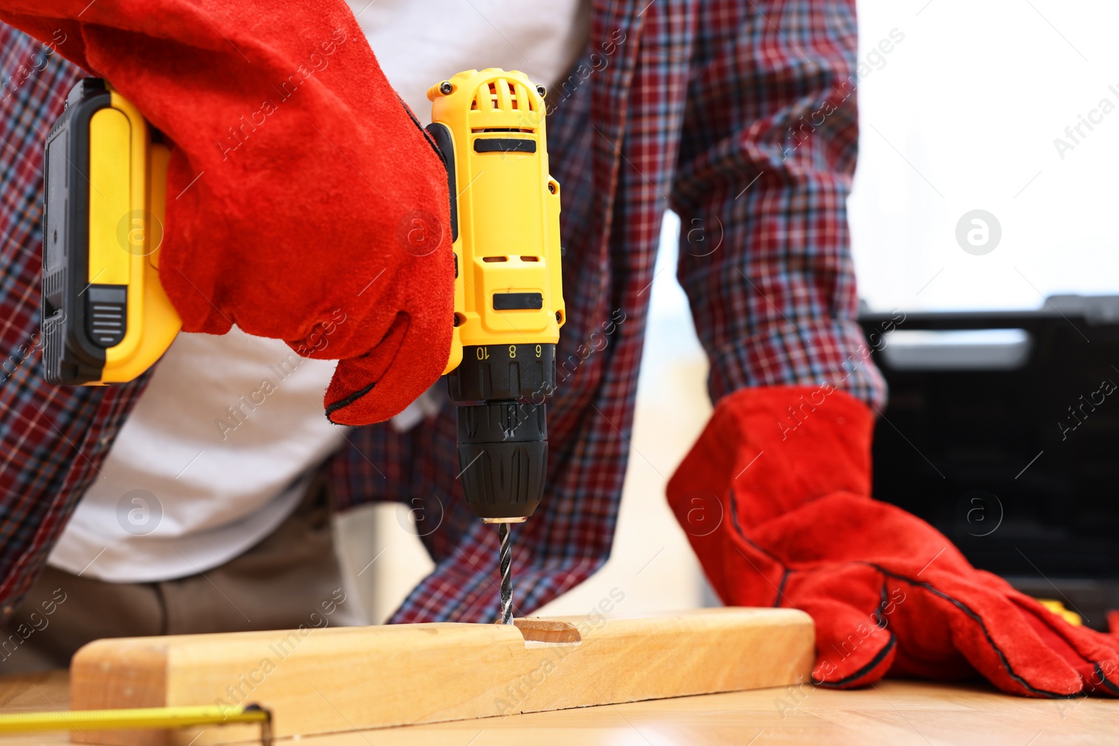 Photo of Young handyman working with electric drill at table in workshop, closeup