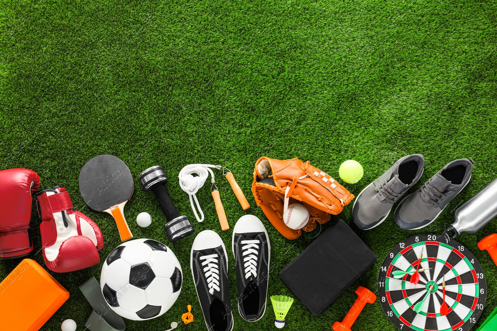 Photo of Different sport equipment and sneakers on green grass, flat lay. Space for text